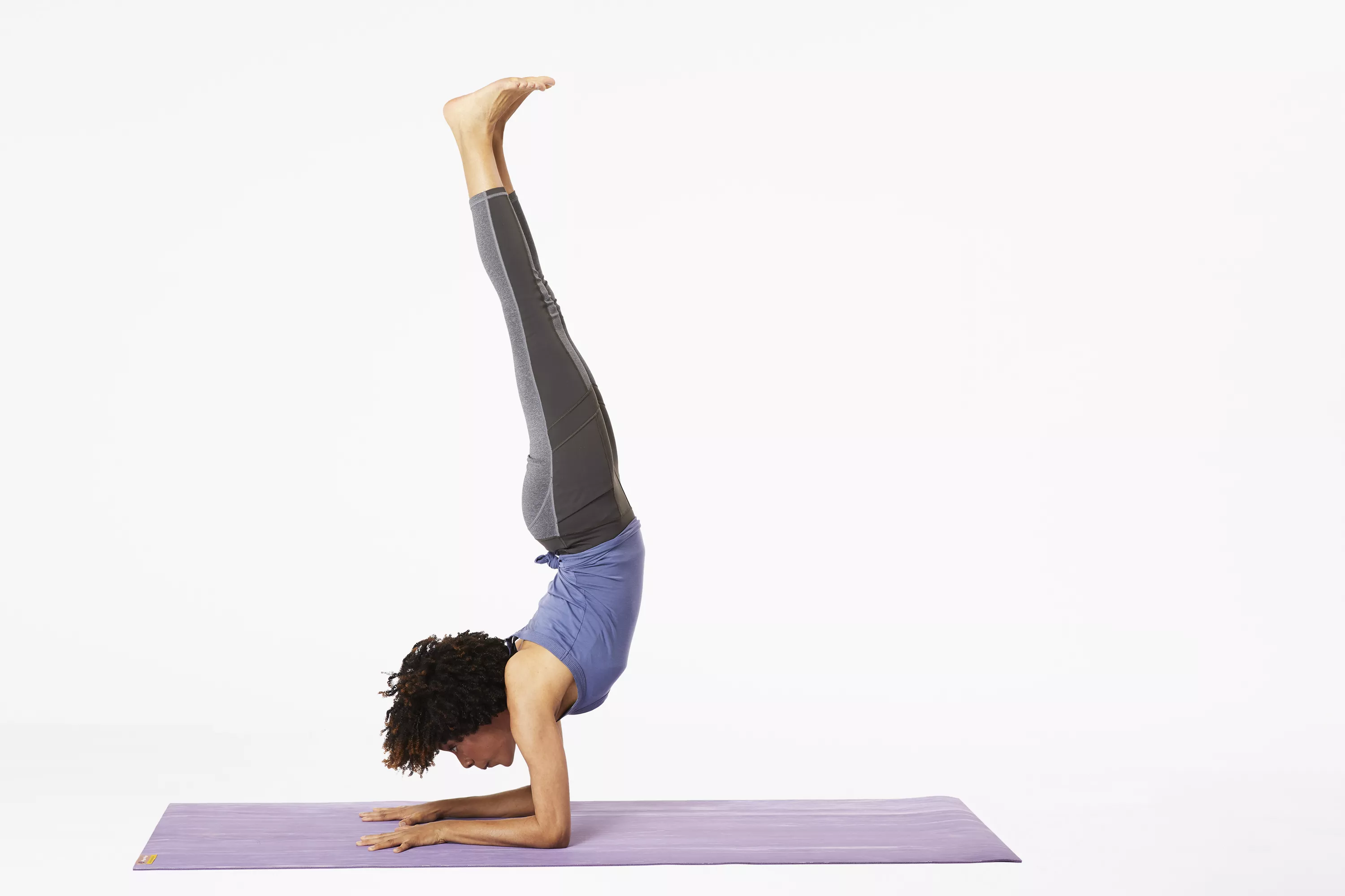 Woman on yoga mat doing forearm stand