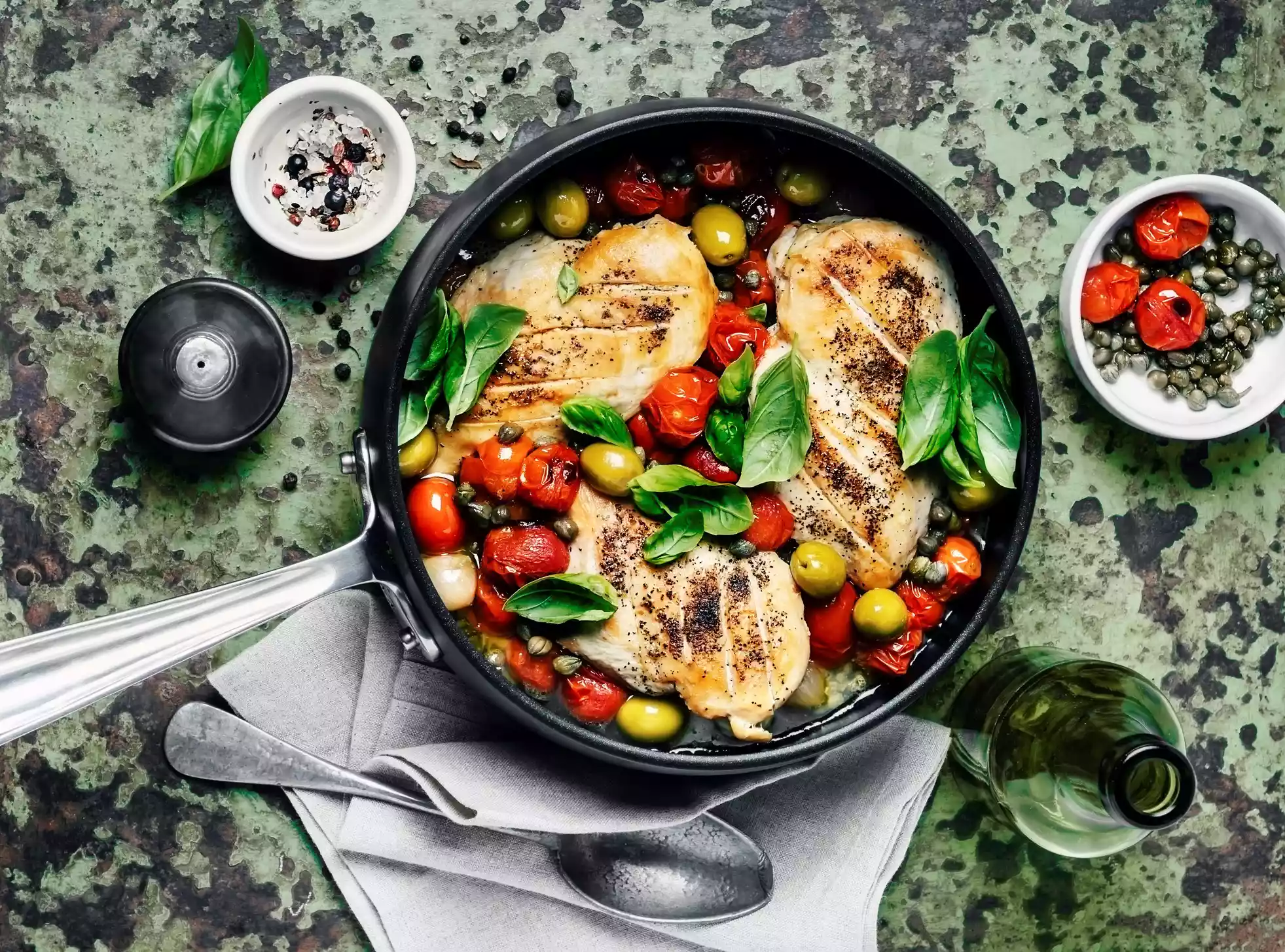 Chicken in a frying pan with tomatoes, spinach leaves, and olives