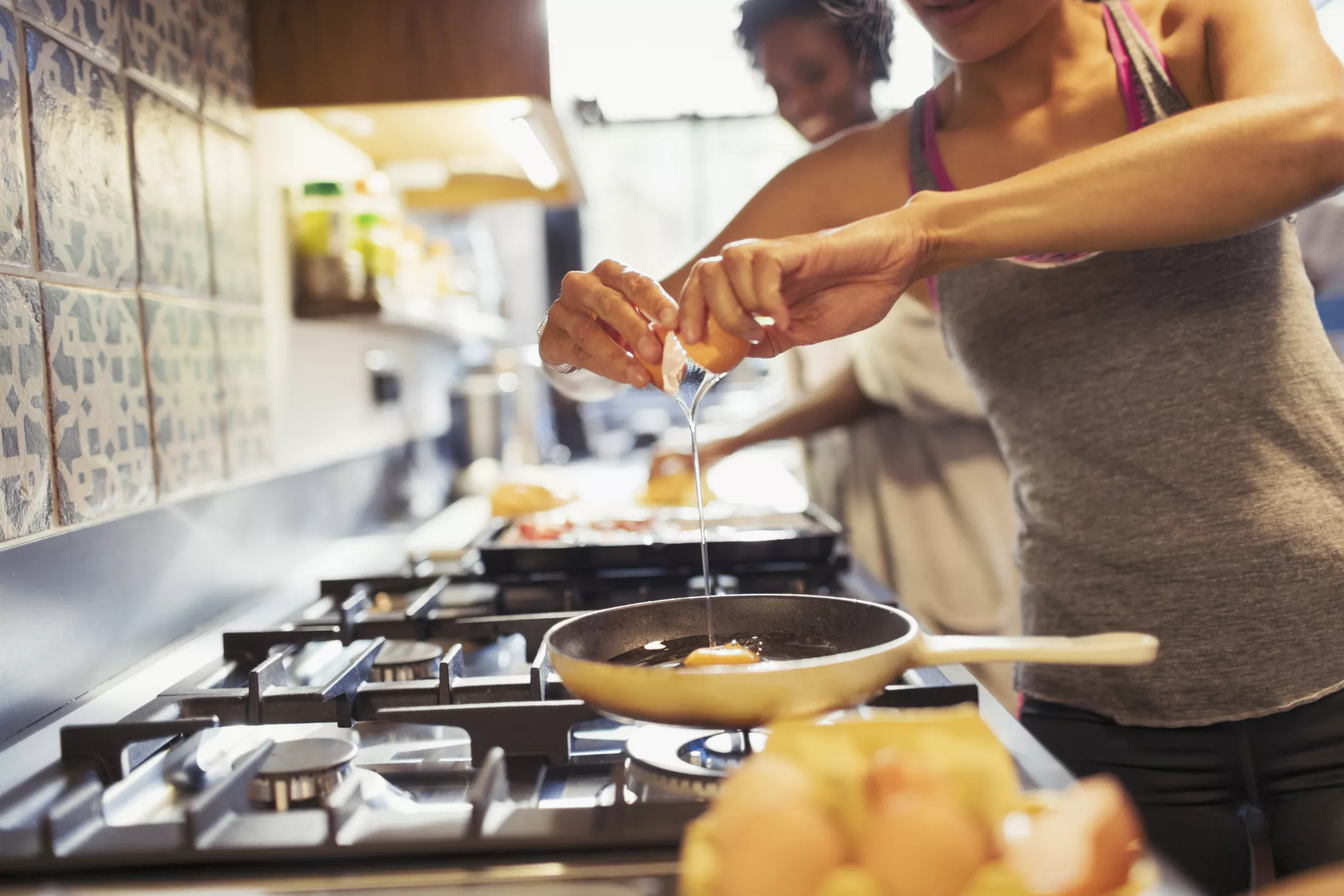 Young woman cracking egg over skillet on stove in kitchen